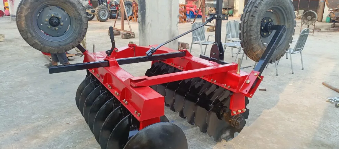 Red disc harrow with black disc gangs and raised transport wheels in a machinery area